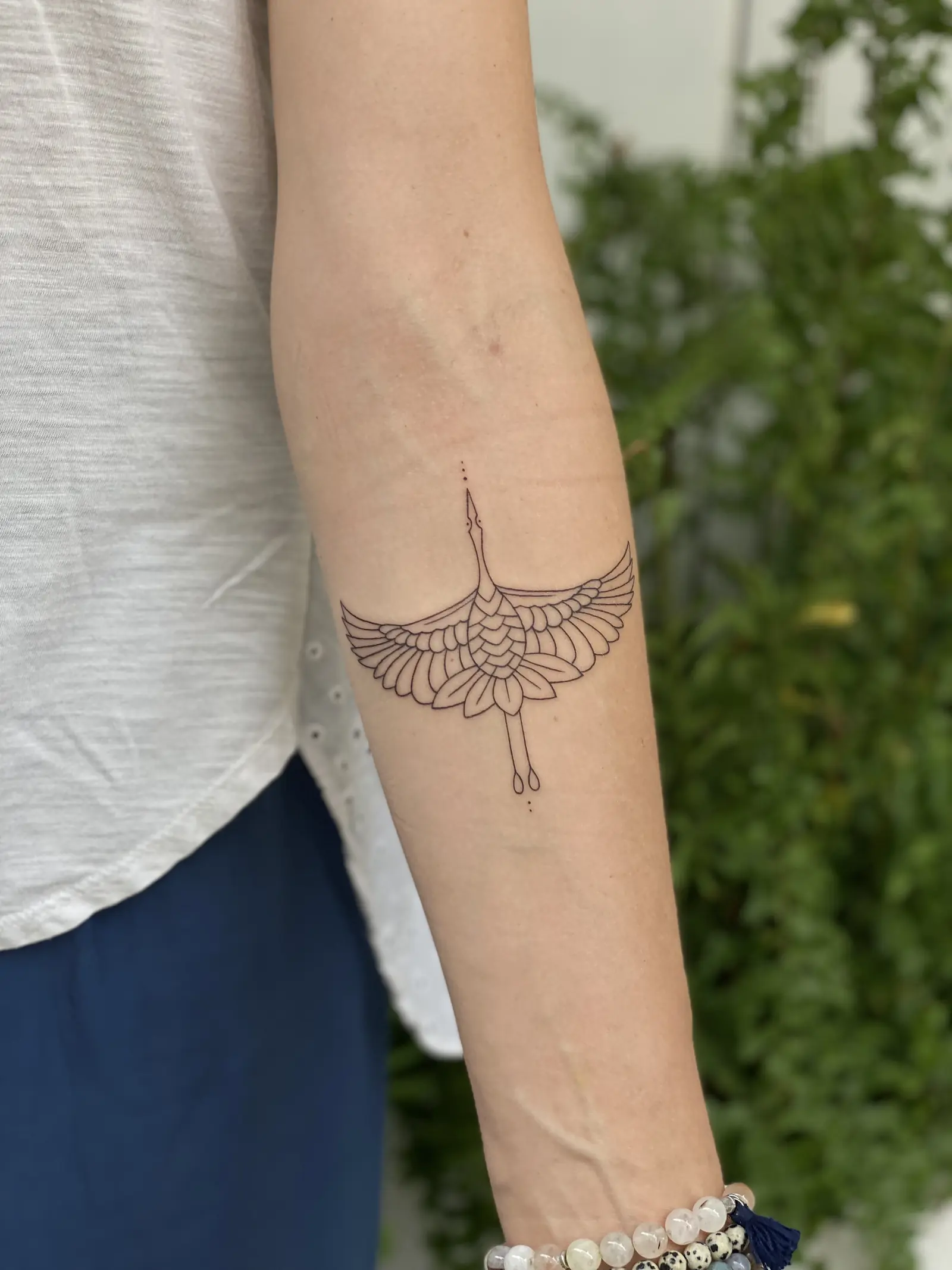Fine line crane bird with spread wings tattoo on the forearm, done in Cartagena