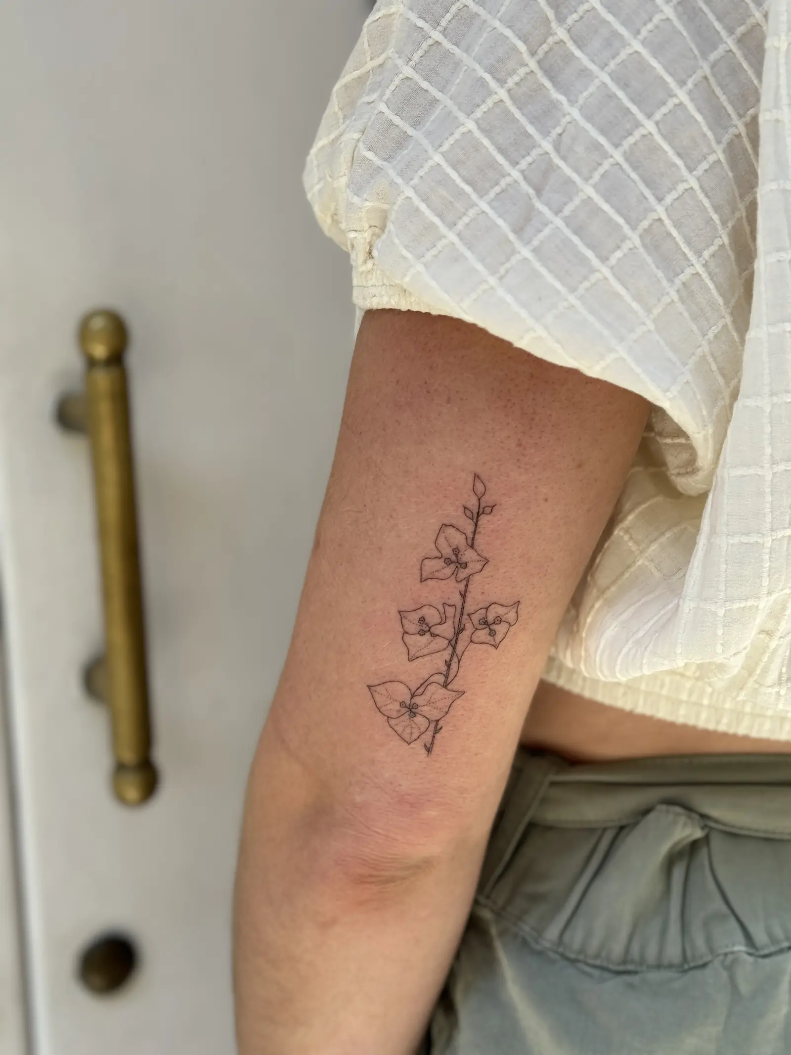 Tatuaje fine line de una rama con flores en el brazo, hecho en Cartagena