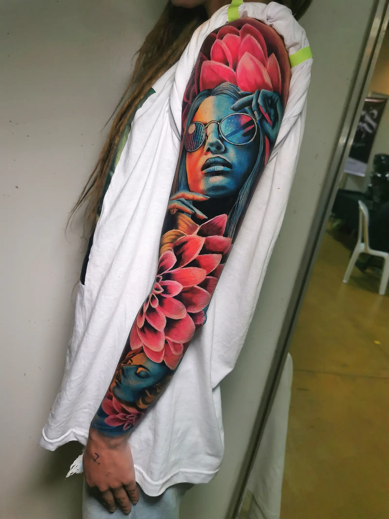 Tatuaje de manga a color con una mujer con gafas de sol y flores de dalia rosadas, hecho en Cartagena