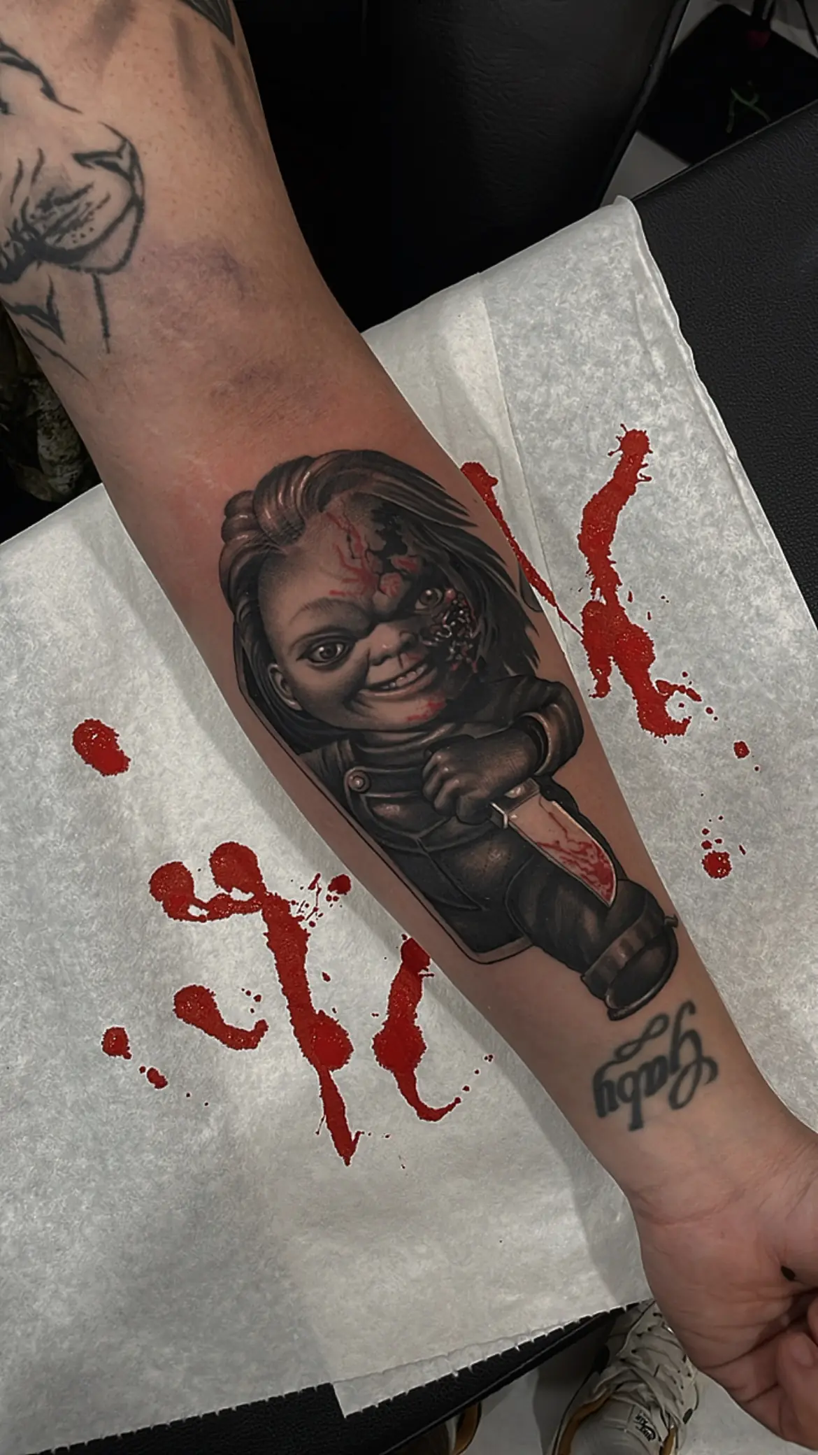 Tatuaje realista de Chucky con un cuchillo en el antebrazo, hecho en Cartagena