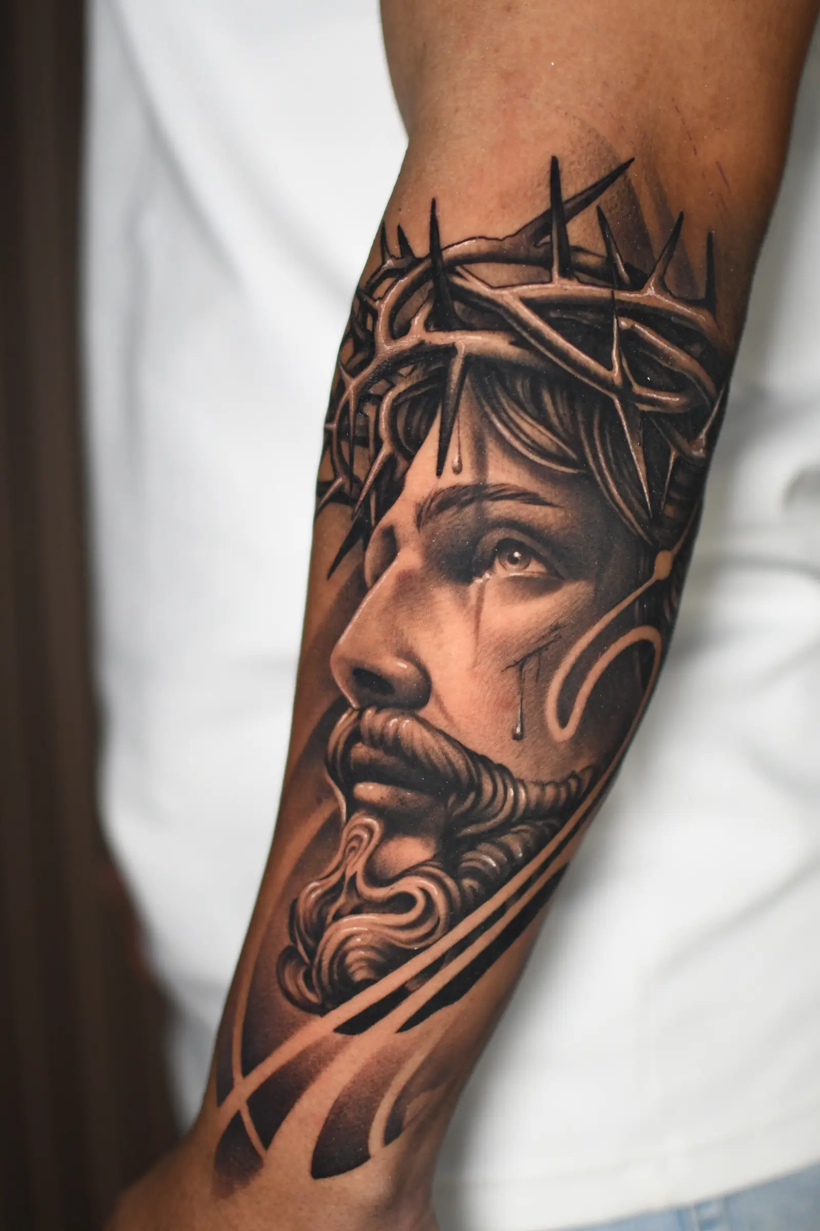 Tatuaje realista en blanco y negro de Jesús con corona de espinas en el antebrazo, hecho en Cartagena