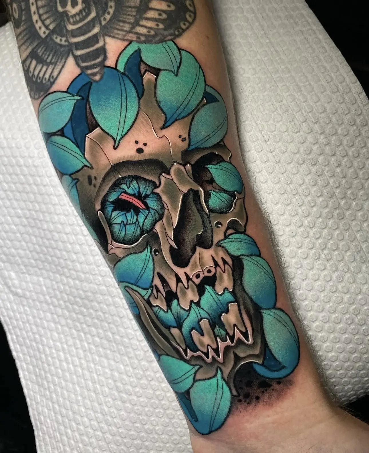 Tatuaje tradicional a color de una calavera con hojas turquesas, hecho en Cartagena